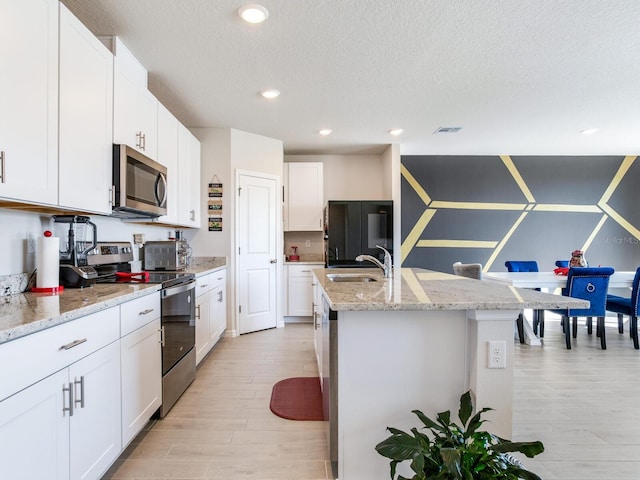 kitchen with appliances with stainless steel finishes, white cabinetry, a kitchen island with sink, and sink