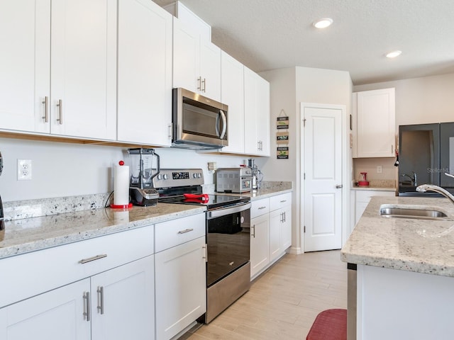 kitchen featuring stainless steel appliances, light stone countertops, white cabinetry, and sink