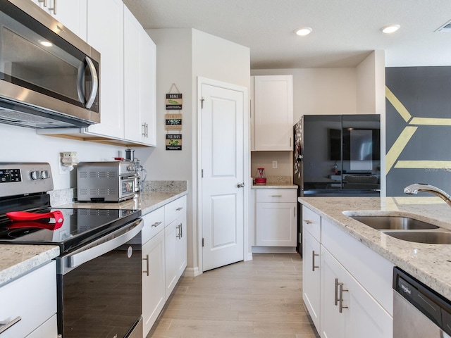 kitchen featuring stainless steel appliances, sink, white cabinets, light stone counters, and light wood-type flooring