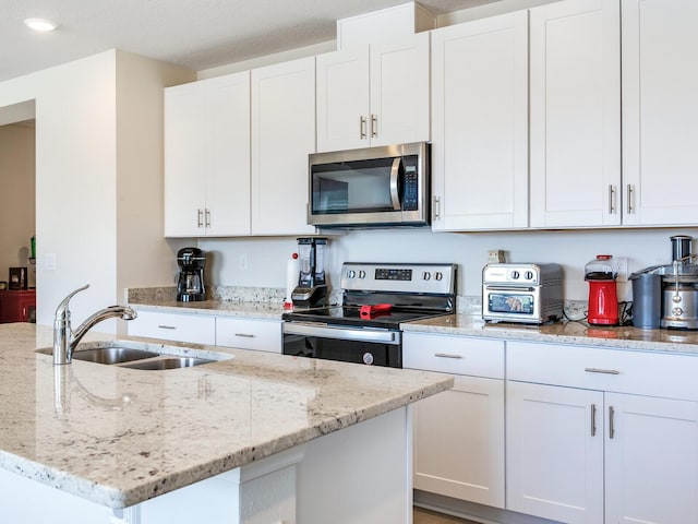 kitchen with stainless steel appliances, white cabinetry, sink, and light stone counters