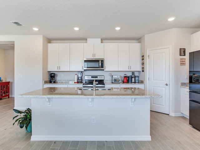 kitchen featuring light stone counters, an island with sink, appliances with stainless steel finishes, and white cabinetry