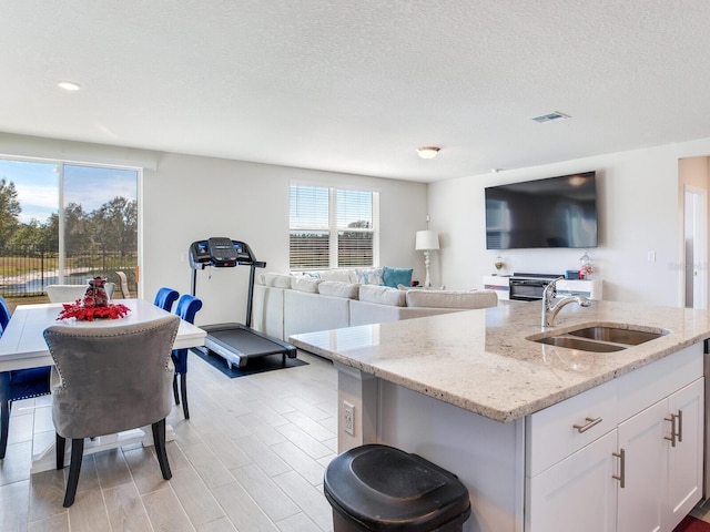 kitchen featuring sink, white cabinetry, a textured ceiling, light stone counters, and a center island with sink