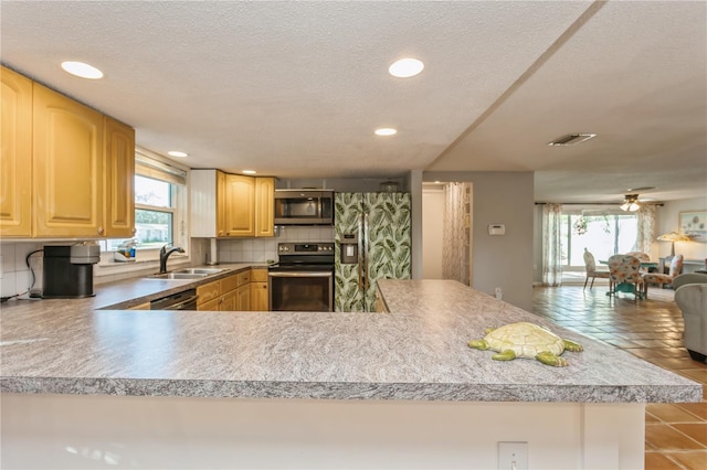 kitchen featuring kitchen peninsula, ceiling fan, stainless steel appliances, backsplash, and light brown cabinetry