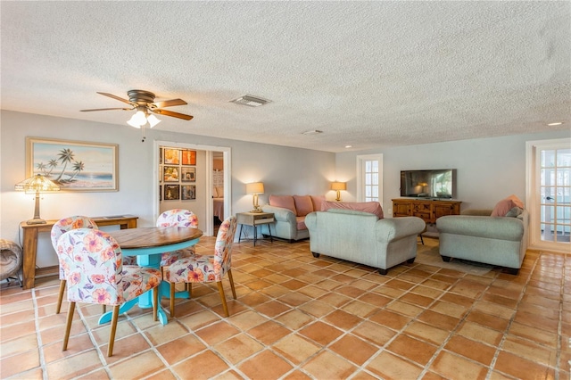 living area with a ceiling fan, visible vents, and a textured ceiling