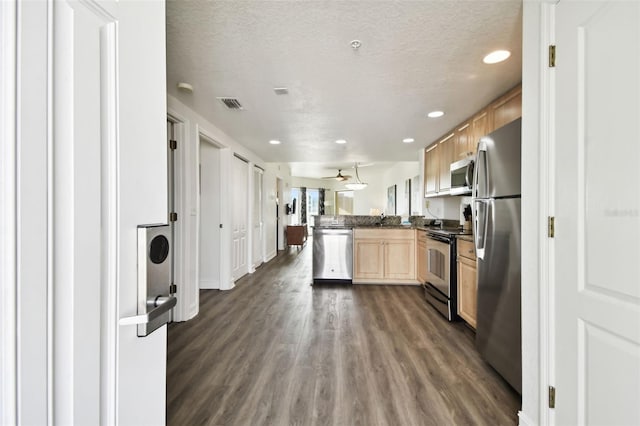 kitchen featuring dark wood-type flooring, a textured ceiling, light brown cabinetry, appliances with stainless steel finishes, and kitchen peninsula