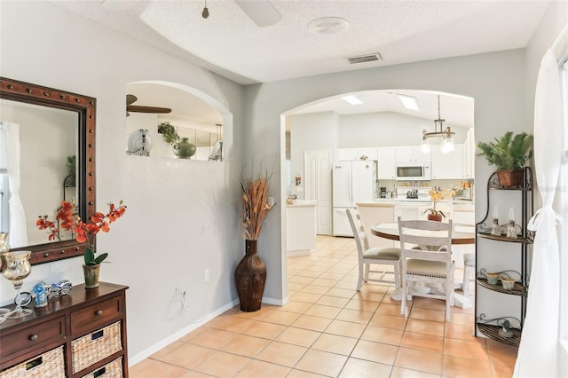 tiled dining space with a textured ceiling, vaulted ceiling, and ceiling fan