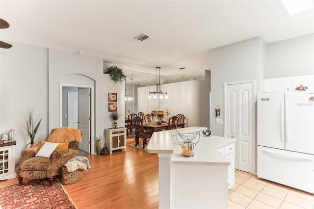 kitchen with white cabinetry, a center island, white refrigerator, light hardwood / wood-style floors, and pendant lighting