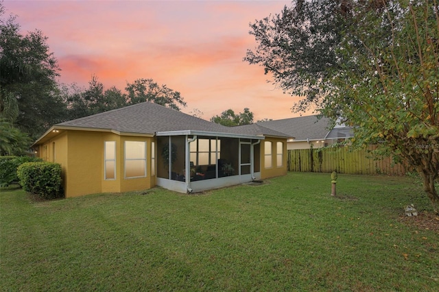 back house at dusk with a sunroom and a yard