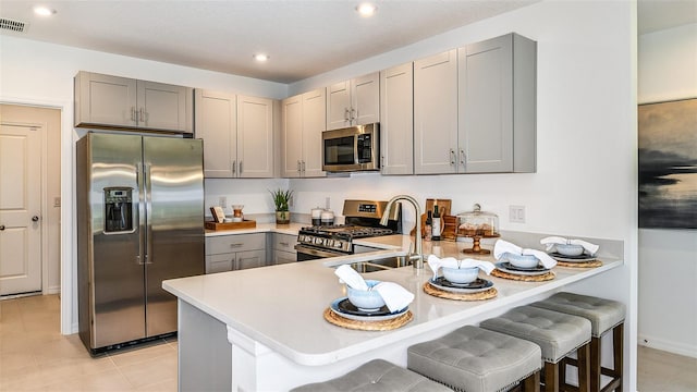 kitchen with gray cabinetry, sink, appliances with stainless steel finishes, a kitchen bar, and kitchen peninsula