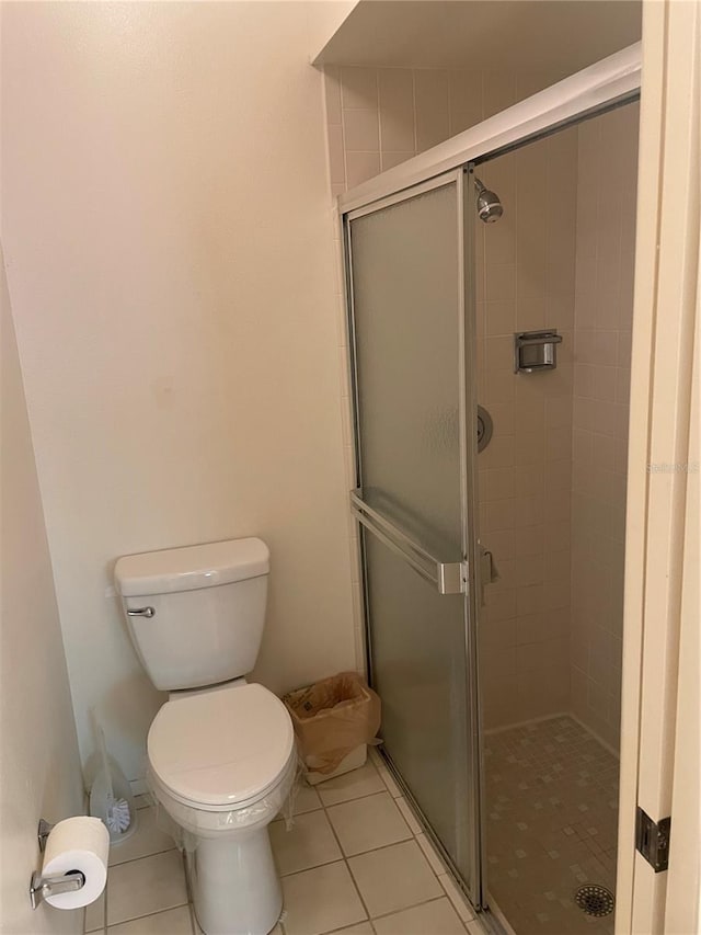 bathroom featuring tile patterned flooring, a shower with door, and toilet