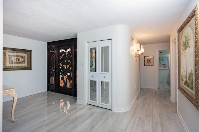 corridor featuring light hardwood / wood-style floors, a textured ceiling, and an inviting chandelier