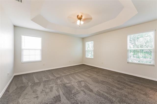 spare room with a tray ceiling, plenty of natural light, and dark carpet