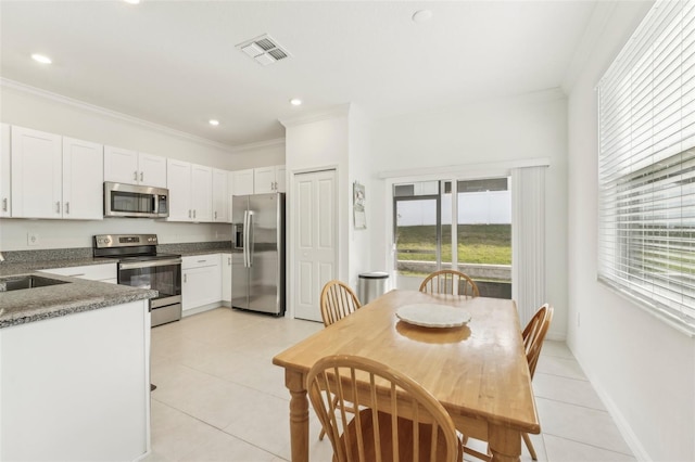 kitchen featuring white cabinets, appliances with stainless steel finishes, dark stone countertops, ornamental molding, and light tile patterned floors