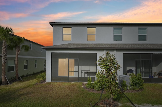 back house at dusk featuring a lawn, cooling unit, and a sunroom