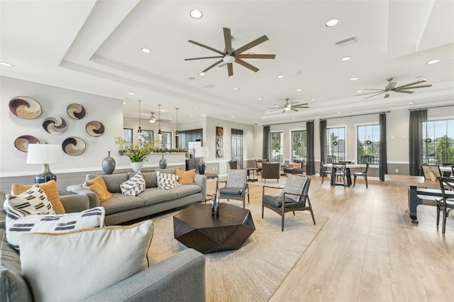 living room featuring ceiling fan, a healthy amount of sunlight, light wood-type flooring, and a tray ceiling