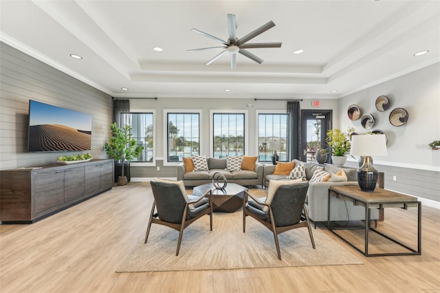 living room featuring ceiling fan, light hardwood / wood-style flooring, and a tray ceiling