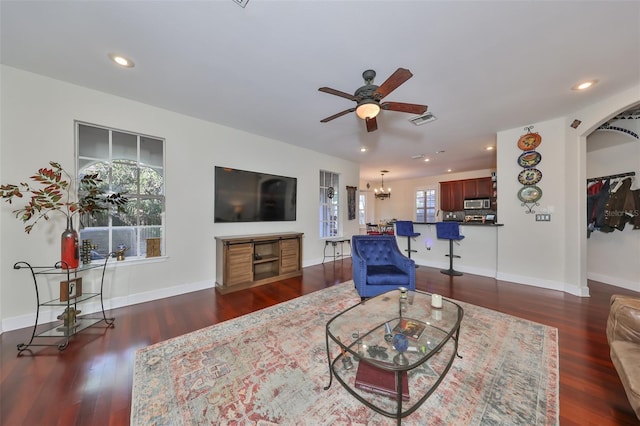 living room with ceiling fan with notable chandelier and dark hardwood / wood-style flooring