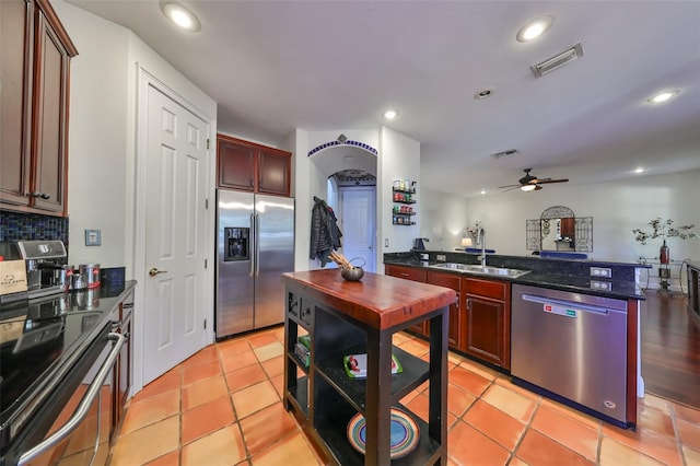 kitchen with sink, dark stone countertops, light tile patterned floors, ceiling fan, and stainless steel appliances