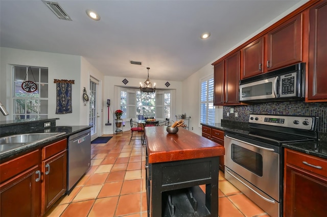 kitchen with appliances with stainless steel finishes, tasteful backsplash, sink, hanging light fixtures, and a center island