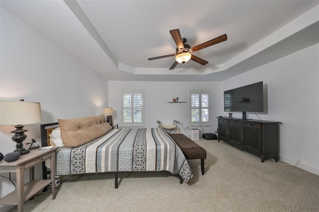 carpeted bedroom with ceiling fan and a tray ceiling