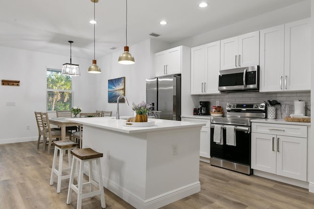 kitchen with white cabinets, decorative backsplash, hanging light fixtures, a center island with sink, and appliances with stainless steel finishes