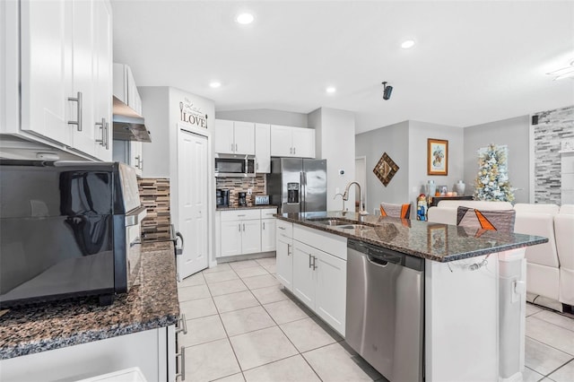 kitchen with dark stone counters, stainless steel appliances, sink, white cabinetry, and an island with sink