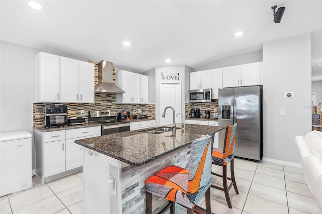 kitchen with sink, wall chimney range hood, an island with sink, vaulted ceiling, and appliances with stainless steel finishes