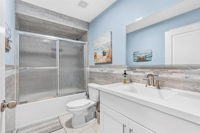 full bathroom featuring vanity, bath / shower combo with glass door, tile patterned flooring, toilet, and tile walls