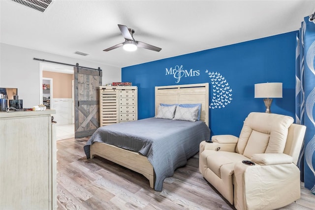 bedroom with light wood-type flooring, a barn door, and ceiling fan