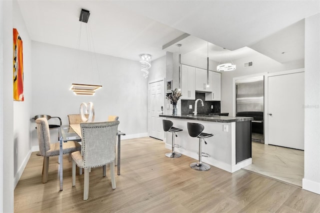 kitchen with white cabinets, decorative backsplash, light hardwood / wood-style flooring, and pendant lighting