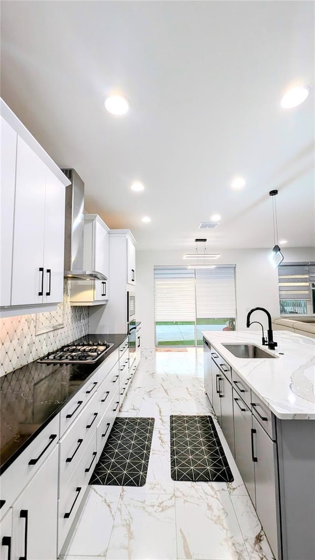 kitchen featuring tasteful backsplash, wall chimney range hood, pendant lighting, white cabinets, and sink