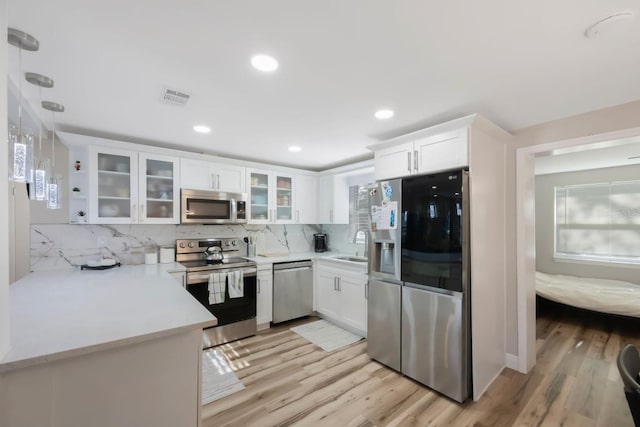 kitchen featuring decorative backsplash, appliances with stainless steel finishes, light wood-type flooring, white cabinets, and hanging light fixtures