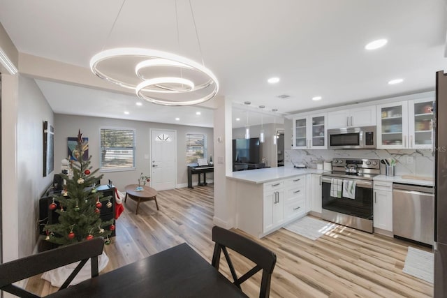 kitchen with tasteful backsplash, stainless steel appliances, decorative light fixtures, light hardwood / wood-style flooring, and white cabinets