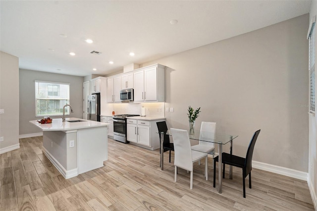 kitchen with white cabinetry, sink, stainless steel appliances, a center island with sink, and light wood-type flooring