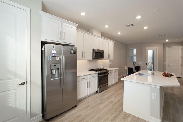 kitchen with white cabinets, sink, stainless steel appliances, and an island with sink