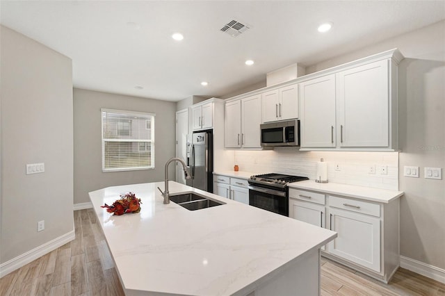 kitchen featuring sink, light wood-type flooring, an island with sink, and appliances with stainless steel finishes