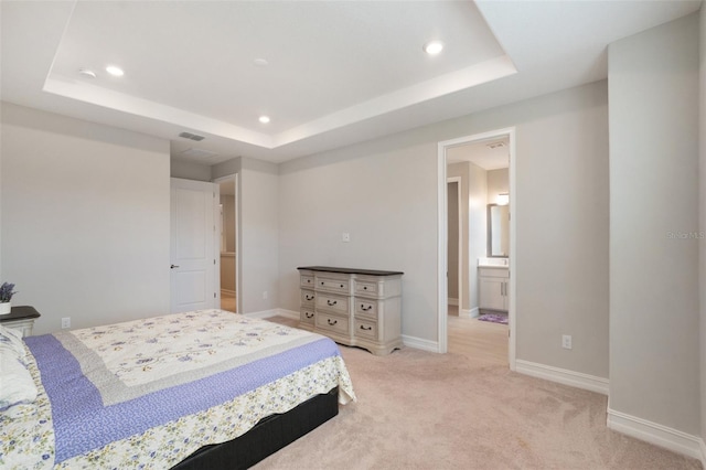 bedroom featuring a tray ceiling, ensuite bath, and light colored carpet