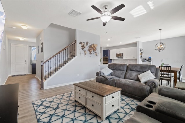 living room featuring ceiling fan with notable chandelier and light hardwood / wood-style floors