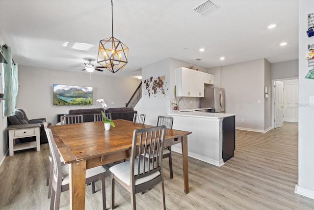 dining space featuring light hardwood / wood-style flooring, ceiling fan with notable chandelier, and sink