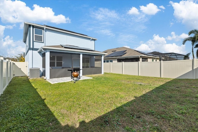 rear view of house with solar panels, central AC unit, a lawn, and a sunroom