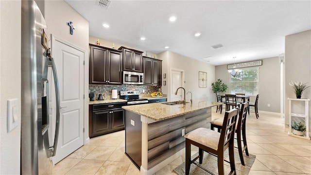 kitchen featuring a kitchen island with sink, sink, decorative backsplash, light stone countertops, and stainless steel appliances