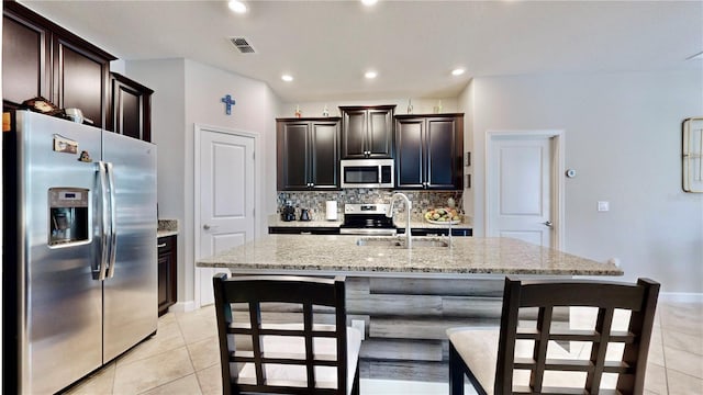 kitchen featuring a center island with sink, sink, light stone countertops, light tile patterned floors, and appliances with stainless steel finishes