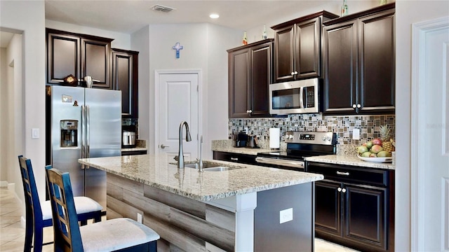 kitchen with a kitchen bar, appliances with stainless steel finishes, backsplash, a kitchen island with sink, and sink