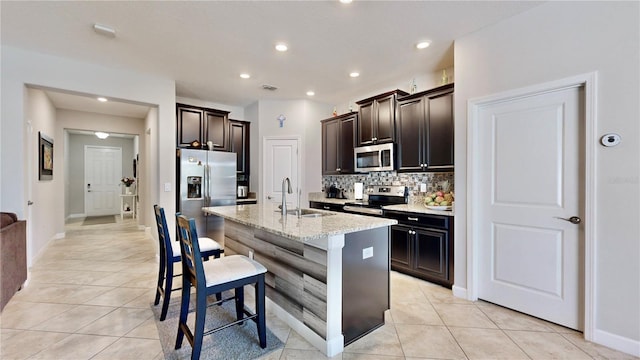 kitchen featuring sink, light stone counters, an island with sink, decorative backsplash, and appliances with stainless steel finishes