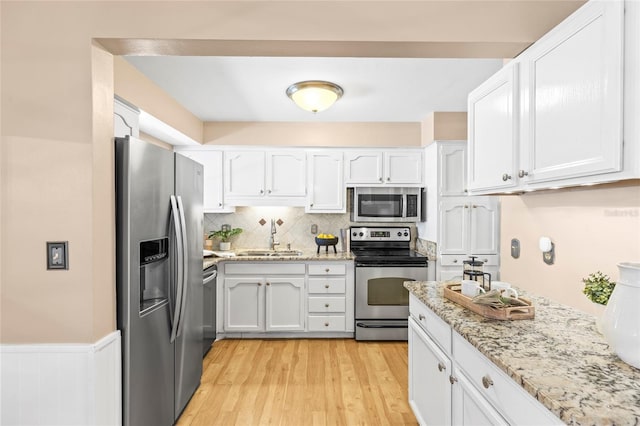 kitchen featuring white cabinetry, sink, tasteful backsplash, light hardwood / wood-style floors, and appliances with stainless steel finishes