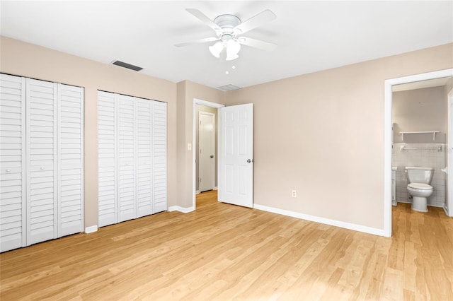 unfurnished bedroom featuring ensuite bath, ceiling fan, tile walls, two closets, and light wood-type flooring