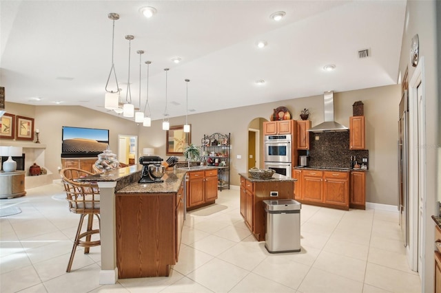 kitchen featuring lofted ceiling, a spacious island, wall chimney range hood, decorative light fixtures, and a breakfast bar area