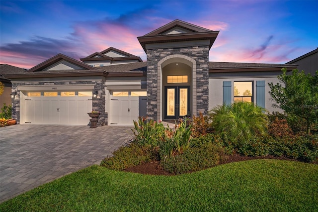 view of front of home featuring a garage, stone siding, decorative driveway, stucco siding, and a front lawn