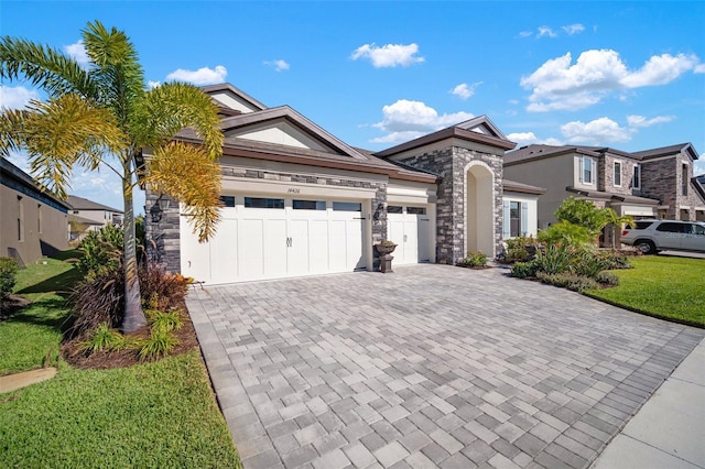 view of front of property featuring a garage, stone siding, decorative driveway, and a front yard