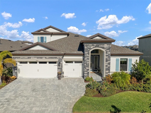 view of front of property featuring decorative driveway, stucco siding, a shingled roof, an attached garage, and stone siding